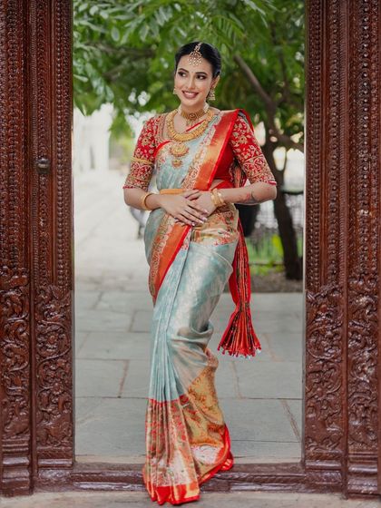 A full-length shot of the bride standing in a traditional doorway, showcasing her elegant saree and complete bridal look.