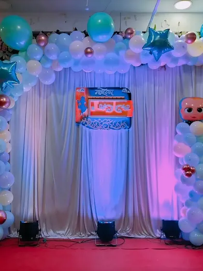 A Boss Baby themed stage for a naming ceremony. The setup includes a balloon arch and columns with character cutouts, all highlighted with stage lighting.