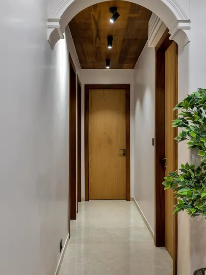An elegant hallway with a dark wood-paneled ceiling and track lighting. The clean white walls and simple wooden doors create a modern and sophisticated look.