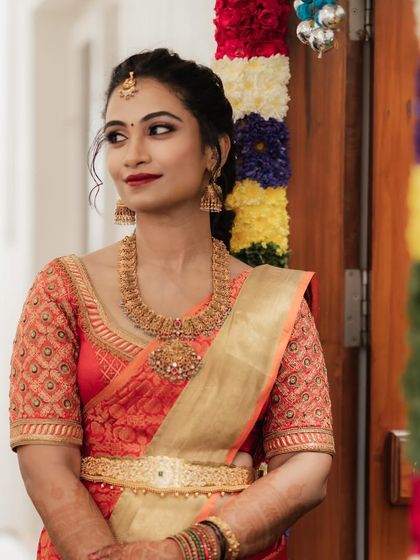 A beautiful portrait of Dr. Pooja at her bangle ceremony, showcasing her elegant updo and radiant makeup against the backdrop of festive flower decorations.
