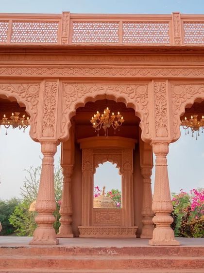 A wide shot that captures the impressive scale of the rajwada. The couple stands on the steps, framed by the grand arches, creating a sense of distance and majesty.