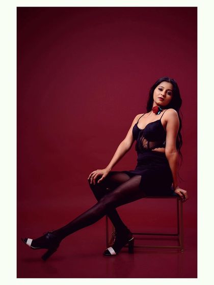 A full-length shot of a model in a black dress against a red background. The pose is strong and the color contrast is striking.