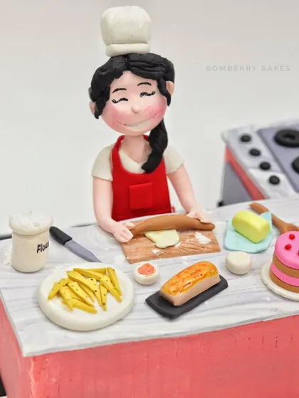 A close-up of the "Kitchen Queen" figurine, happily rolling dough in her miniature kitchen.