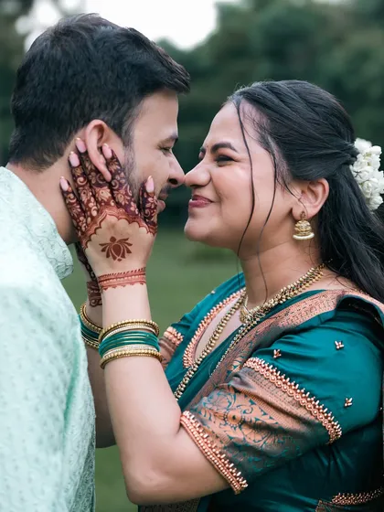 An intimate and tender pre-wedding portrait. The bride's hands, adorned with henna, gently frame his face in a moment of quiet connection.