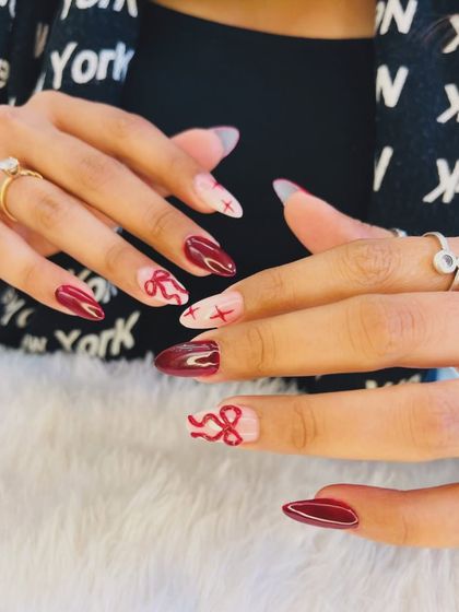 A chic and subtle way to celebrate the season of love. This design features deep red nails with delicate, hand-painted red bow and 'XO' accents on a sheer pink base.