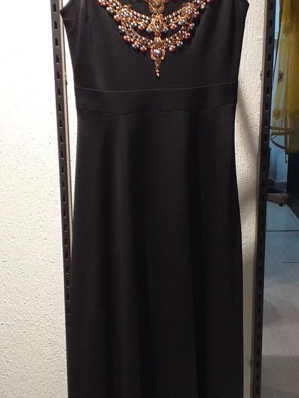 A classic black sheath dress elevated by an ornate, jewel-encrusted neckline. This is a perfect cocktail dress that combines simplicity with a touch of opulence.