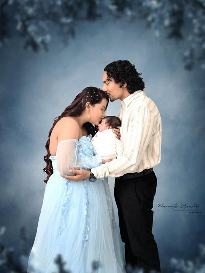 A dreamy and romantic newborn portrait. The parents tenderly kiss their baby's head, surrounded by a soft, ethereal blue background that makes the moment feel magical.
