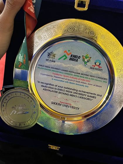A closer look at the prize. The Gold medal and engraved plaque from the Khelo India University Games, a testament to dedication.