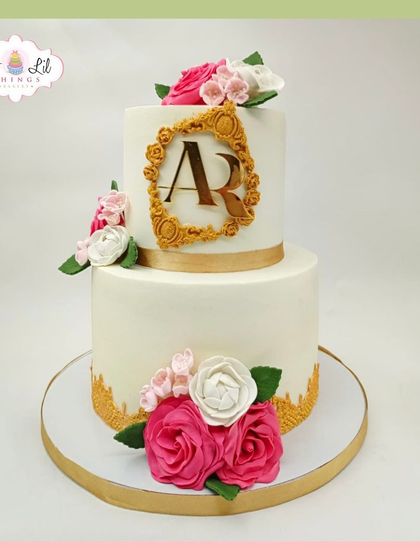 An elegant two-tiered cake with a custom "AR" monogram, decorated with beautiful pink and white sugar roses.