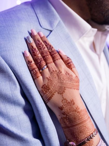 A simple, elegant shot of the bride's hand, adorned with henna and her ring, resting on the groom's suit. It speaks of love, trust, and partnership.