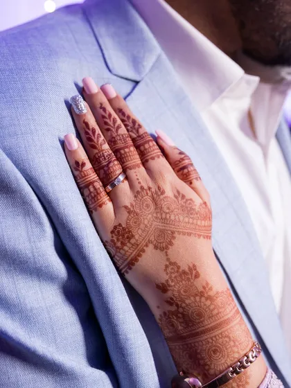 A close-up of the bride's hand with mehndi, resting on the groom's suit.