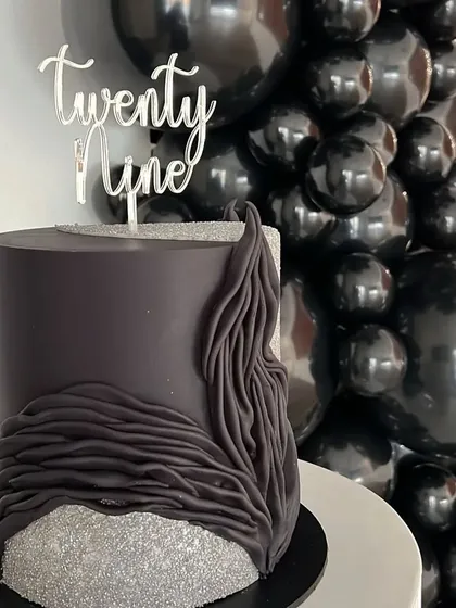 A custom cake designed to match the all-black theme, featuring a modern textured design and a 'Twenty Nine' topper.