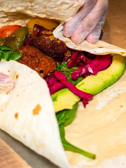 A close-up of a falafel wrap being assembled, showing the vibrant colors of the fresh ingredients like avocado and pickled cabbage. This builds trust by showing what's inside.