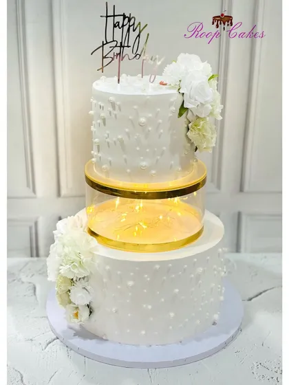 Simplicity and light. This beautiful two-tier white cake features a lighted separator tier and is decorated with delicate pearl-like dots and fresh white flowers.