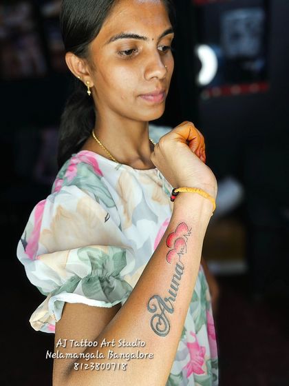 A lovely "Aruna" name tattoo on the forearm with a cloud of hearts.