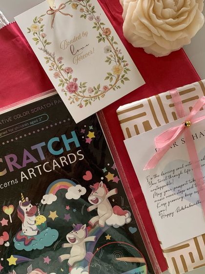 A sweet and thoughtful Rakhi gift set. It includes a personalized letter, unicorn-themed scratch art cards for a younger sister, and a 'Bonded by Love Forever' card.