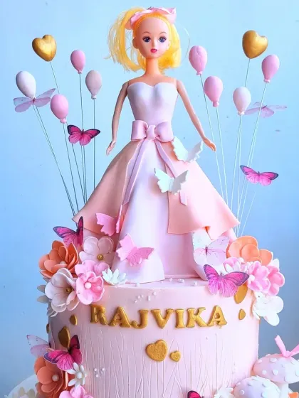 A beautiful Barbie doll cake with a textured buttercream skirt and a fondant dress topper. The addition of balloon and butterfly wires adds height and a sense of celebration.