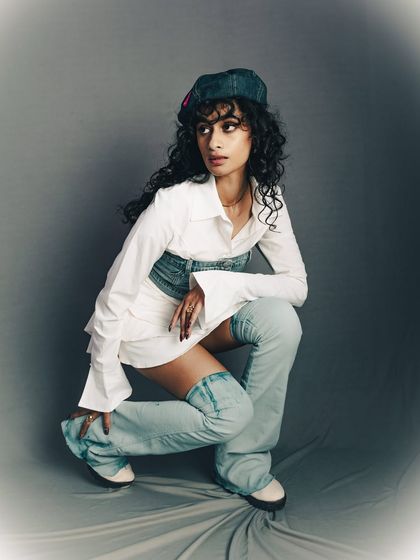 A dynamic crouching pose that highlights the unique silhouette of the outfit, including the thigh-high denim boots.