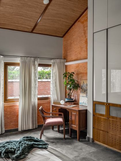 Another view of the bedroom with the terracotta wall, showing how the space feels cohesive yet has distinct zones for rest and work. The vaulted ceiling adds to the room's spacious feel.
