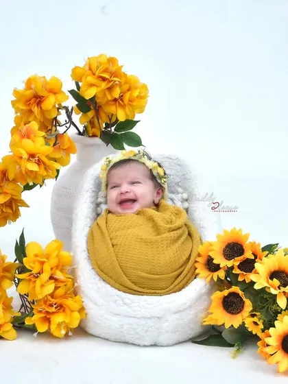 Capturing a precious, happy smile from a newborn baby swaddled in a yellow wrap. The scene is decorated with bright sunflowers and yellow flowers for a cheerful and sunny portrait.