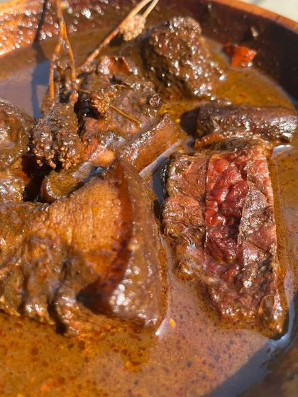 A close-up of the rich, dark Smoked Pork Anishi curry, showing the tender pieces of meat and the deep color of the gravy.