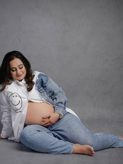 A gentle and introspective solo portrait, with the mother-to-be cradling her bump in a casual, modern setting.