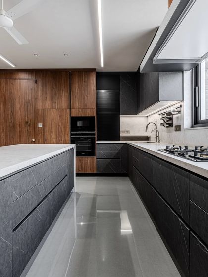 A full view of the handle-less island kitchen in Ahmedabad, showing the beautiful balance between the dark, textured cabinets and the light, continuous quartz surfaces.