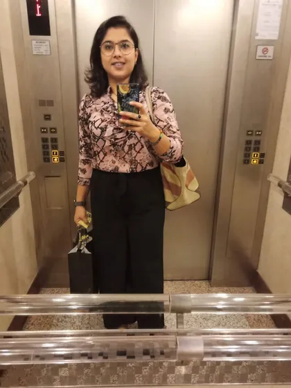 An 'after' photo of a client, confidently taking a selfie in an elevator. Her new look, featuring a printed top and wide-leg trousers, reflects her elevated style.