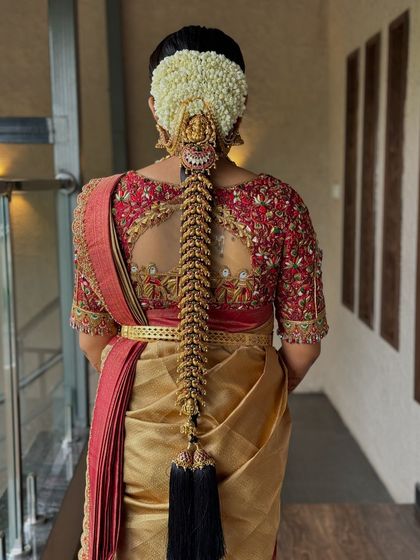 A detailed shot of the back, showcasing a stunning traditional bridal braid with intricate gold accessories and fresh jasmine flowers.