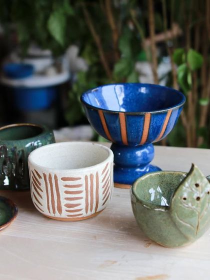 A sophisticated set of student work, including a footed bowl with brilliant blue glaze and cups with carved and painted patterns.