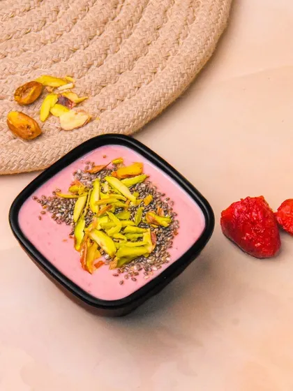 A bowl of strawberry Greek yogurt topped with pistachios and chia seeds, with fresh strawberries on the side. The colors and textures are highlighted by the clean, bright styling.