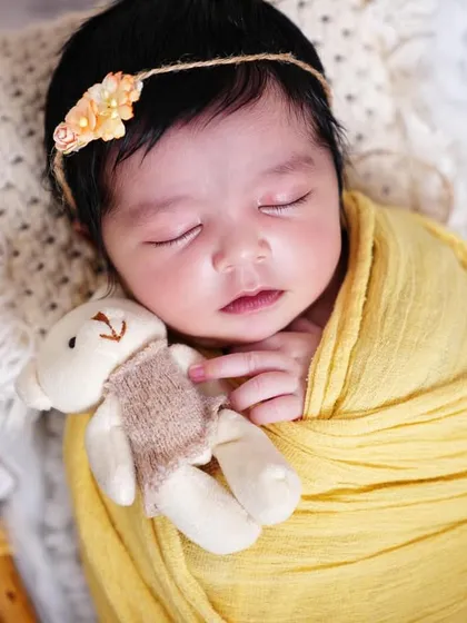 A sweet sleeping baby girl with a floral headband, holding a tiny teddy bear. This home session was so peaceful.