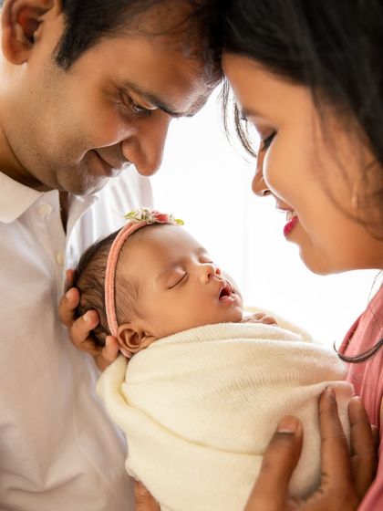 A beautiful family portrait, with parents touching foreheads as they gaze at their sleeping baby girl. A classic pose full of emotion.