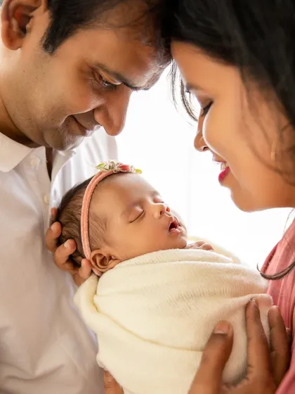 A beautiful family portrait, with parents touching foreheads as they gaze at their sleeping baby girl. A classic pose full of emotion.
