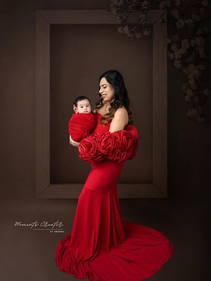 A mother's solo portrait with her newborn. Dressed in a striking red gown, she holds her baby lovingly, framed by a simple, elegant prop that adds a touch of artistic flair.