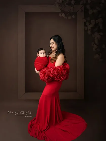 A mother's embrace in a striking red gown. She holds her baby, who is wrapped in a matching red swaddle, creating a bold and powerful portrait of motherhood.