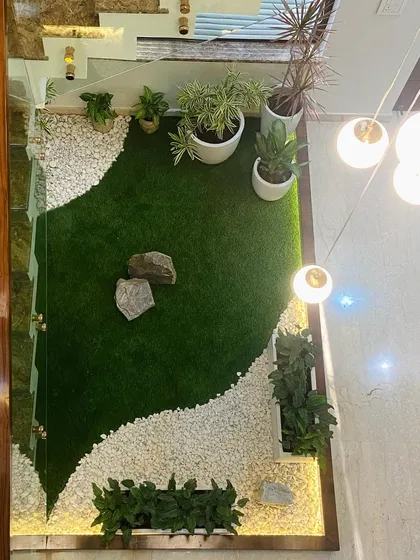 An overhead view of the indoor courtyard garden, showing the careful composition of artificial grass, white pebbles, and natural rocks. The design creates a dynamic, flowing shape that makes the most of the compact space.