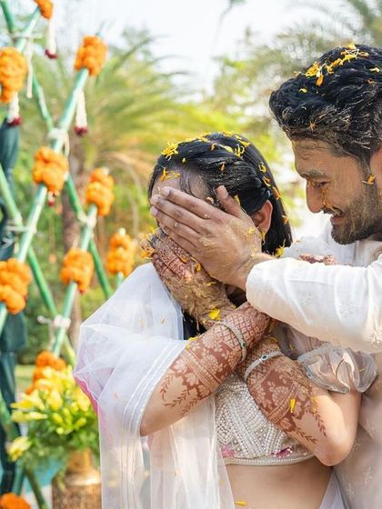 A happy bride playfully applies Haldi to the groom. We design our decor, like this marigold-adorned backdrop, to be the perfect setting for these fun moments.