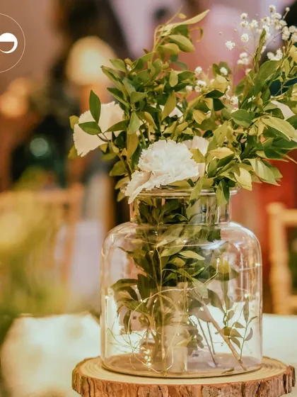 A rustic centerpiece featuring a glass jar of flowers on a wooden slice. This simple detail adds a touch of natural charm to the table setting.