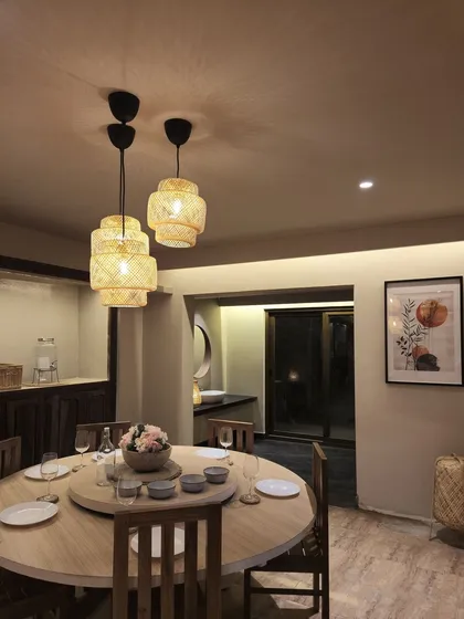 The dining space in our Coorg homestay is illuminated by woven bamboo pendant lights, adding a touch of rustic charm. The round wooden table encourages communal dining, creating a warm and inviting atmosphere for guests.