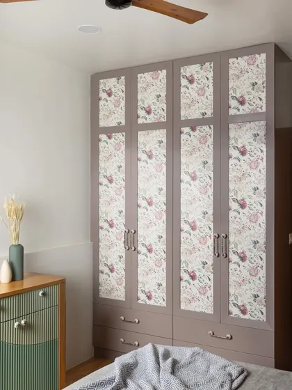 This wardrobe features fabric-sandwiched glass shutters with a floral pattern that complements the room's color palette. It adds subtle texture and vibrancy to the space.