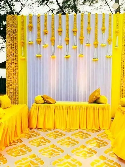 This is a complete Haldi ceremony setup we created, featuring a bright yellow and white theme. We used marigold flower panels and hanging garlands against a clean white backdrop, along with matching seating arrangements, to create a vibrant and photo-ready space.