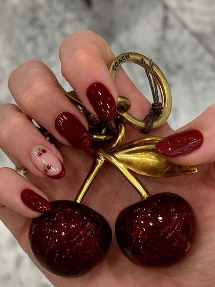 Nail inspiration featuring a deep red manicure with a cherry-themed accent nail.