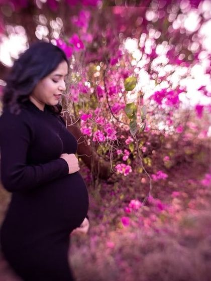 A creative and artistic shot using the vibrant colours of a bougainvillea tree as a natural frame. The mother-to-be in a simple black dress stands out beautifully against the floral backdrop.