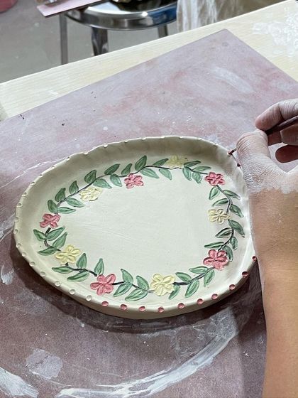 This student is painting a beautiful floral wreath around the rim of their plate. It’s a lovely way to frame the piece.