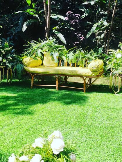 A simple and chic seating arrangement for a mehendi or haldi ceremony, using natural greens and a pop of yellow against the lush lawn.