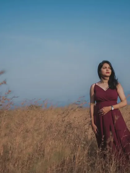 Bathed in the magic of golden hour, this outdoor maternity photo captures a moment of serene reflection. The expecting mother stands in a field of tall grass, her gown flowing, creating a beautiful and cinematic pregnancy portrait against the vast sky.