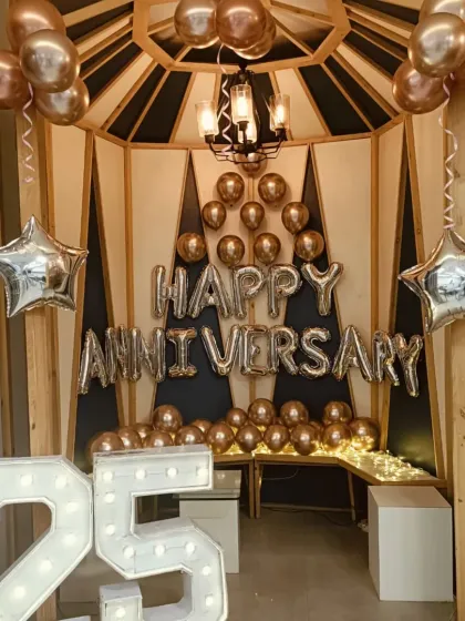 A stylish anniversary party corner. This setup includes a "Happy Anniversary" balloon display, a "25" marquee number, and star-shaped foil balloons inside a wooden gazebo structure.