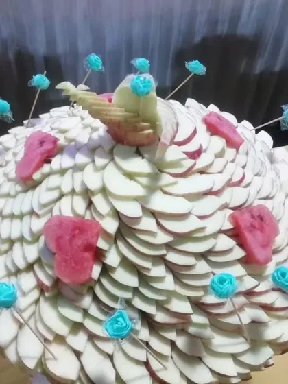 A peacock-inspired fruit sculpture made from sliced apples and decorated with watermelon and sugar roses. This is an example of my bespoke fruit carving services.