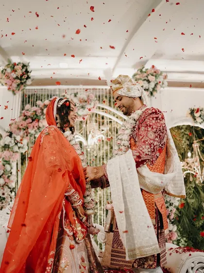 The joy of the Varmala ceremony captured perfectly. The couple exchanges garlands under a shower of rose petals, surrounded by the elegant floral decor of their wedding stage.